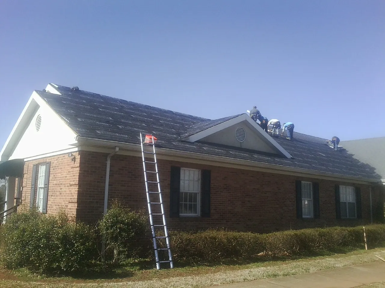 Crew tearing shingles off a brick ranch roof with a ladder set — Emergency Roof Repair work by our crew in Mingo Junction