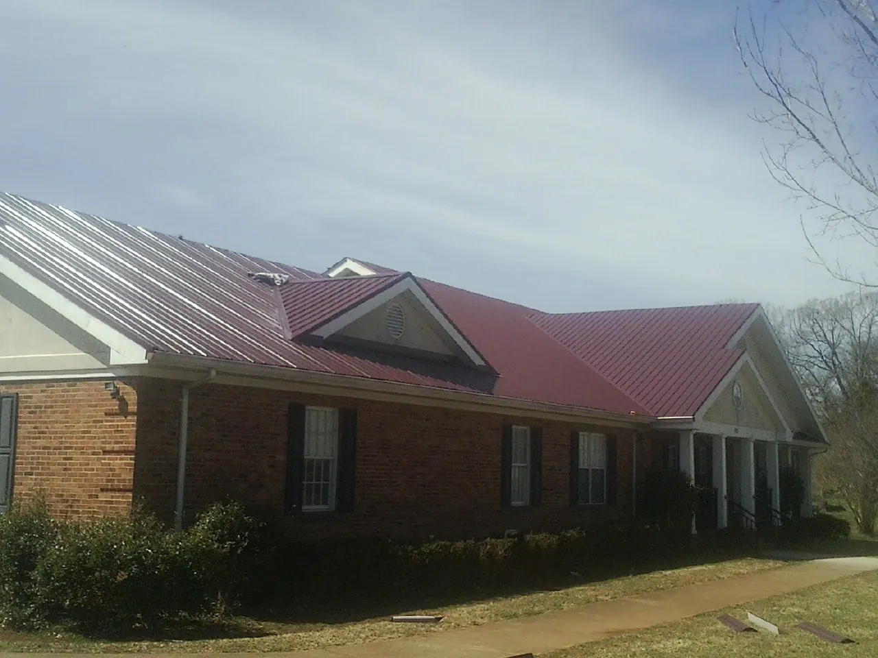 Red metal roof with gabled entries on a long brick building, from a Hail Damage Roof Repair job in Mingo Junction