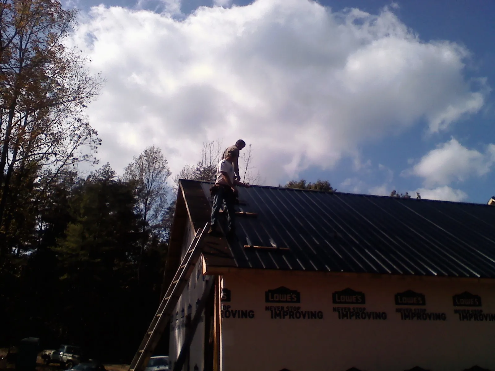 Roofer fastening dark metal panels high against a cloudy sky, from a Roof Inspection job in Mingo Junction
